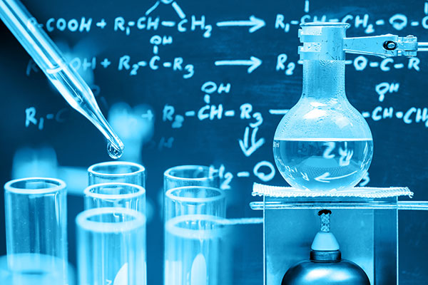 Chemical formulas written on a blackboard in back with chemical lab equipment like test tubes, burner and a round bottom flask
